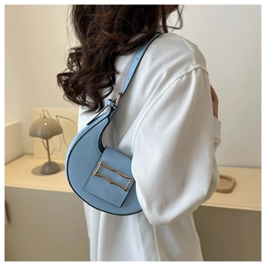 Detail of light blue faux leather crescent bag with matte gold wave buckle on model