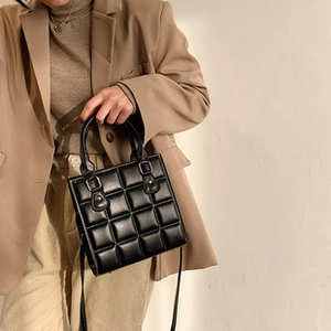 Detail of black quilted PU leather crossbody bag with polished finish and top handle