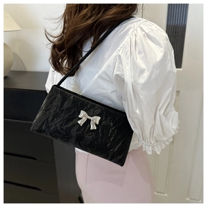 Detail of black pleated crossbody bag with silver bow ornament worn by a model