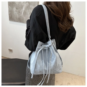Detail of light blue bucket bag with drawstring closure and bow on a model shoulder