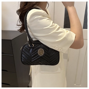 Detail of black quilted shoulder bag with gold embossed medallion and V-shaped stitching
