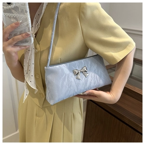 Gros plan sac bandoulière plissé bleu clair avec nœud argenté sur un blazer jaune