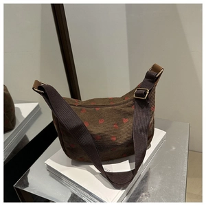 Detail of dark brown corduroy half-moon crossbody bag with red heart embroidery and gold buckle