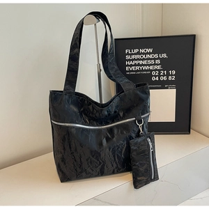 Close-up of black pleated tote bag featuring silver zipper and matching small pouch