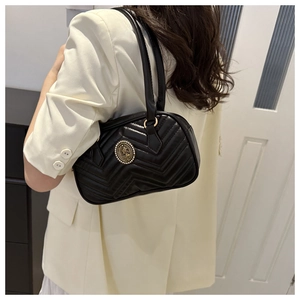 Detail of black quilted shoulder bag featuring an antique gold pearl relief emblem