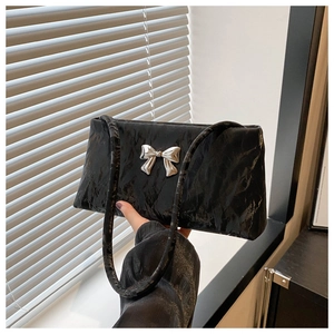 Detail of black pleated bucket bag featuring a silver metal bow accent and textured finish