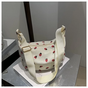 Close-up of white corduroy shoulder bag featuring red strawberry embroidery and gold buckle
