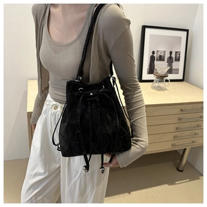 Detail of a black drawstring bucket bag with decorative bow and metallic beads shown on model