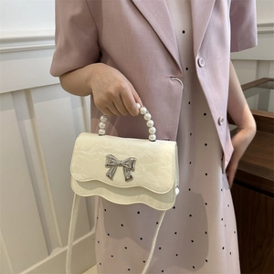 White textured crossbody bag with pearl handle and silver bow worn with a lavender blazer