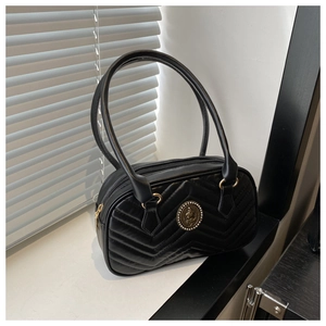 Detail of black quilted shoulder bag featuring V-shaped stitching and a metal emblem