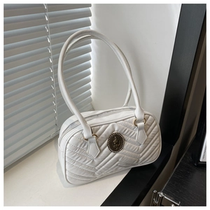 Close-up of white quilted tote bag with V-shaped stitching and vintage metal medallion