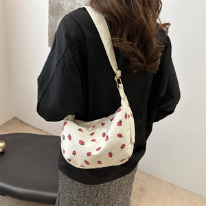 White corduroy crossbody dumpling bag with red strawberry pattern shown on a model