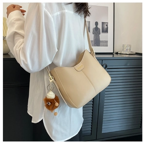 Dettaglio della borsa a tracolla in pelle PU beige con targa dorata e ciondolo a orsetto
