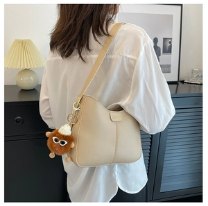 Borsa a secchiello in pelle PU crema con logo fashion e ciondolo a orsetto su un modello