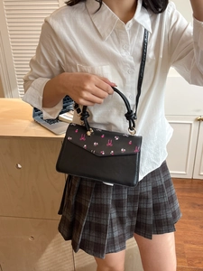 Sac à main tendance en cuir noir avec imprimé floral et garnitures dorées sur un mannequin
