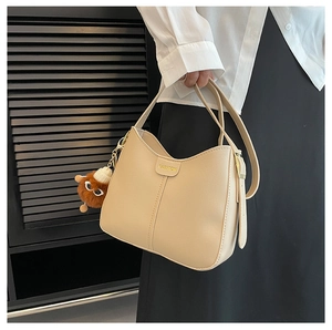 Dettaglio della borsa in ecopelle beige con scritte in metallo e ciondolo a pompon marrone