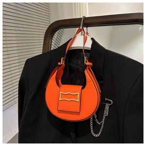 Detail of orange faux leather half-moon bag with gold buckle on black blazer