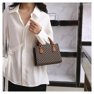 Detail of vintage brown patterned handbag with leather handles held by a model