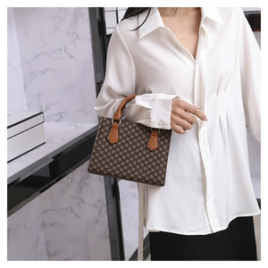Detail of vintage patterned crossbody bag with caramel leather handle held by model