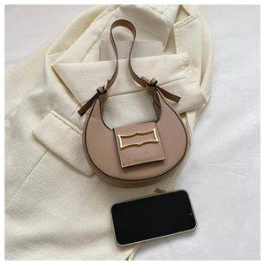 Detail of khaki crescent shoulder bag with golden hardware beside a smartphone for size scale