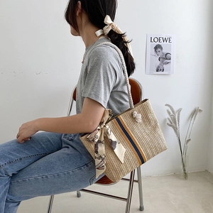 Close-up of woven straw tote bag featuring colorful vertical straps and soft cotton rope handle