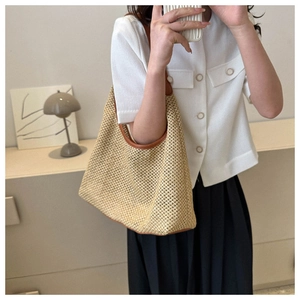 Detail of a natural woven straw tote bag with brown leather trim worn by a model