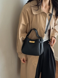 Sac à main élégant en cuir noir grainé avec fermoir doré porté sur un trench-coat