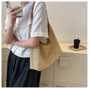 Close-up detail of woven straw beach bag with brown leather trim and shoulder strap