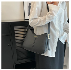 Dettaglio borsa a spalla in pelle nera opaca con scritta Fashion dorata su camicia bianca