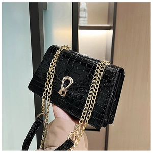 Close-up of black crocodile embossed patent leather with golden metal lock and double chains