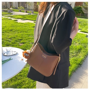 Borsa a spalla in pelle marrone con logo FASHION e ciondolo a pompon in un parco
