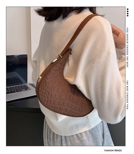 Brown crocodile pattern crescent bag worn on shoulder with white knit sweater