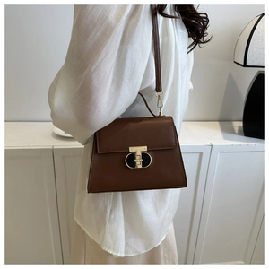 Brown leather crossbody bag with gold T-lock shown on a model in a minimalist setting