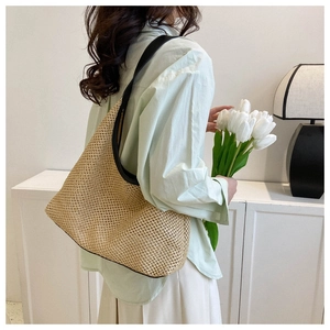 Detail of straw woven tote bag with black leather straps shown on a model shoulder