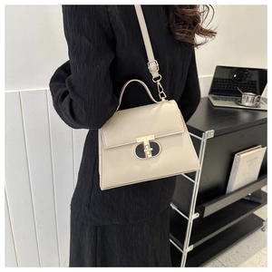 Detail of a beige leather crossbody bag featuring a metal twist lock and a sleek top handle