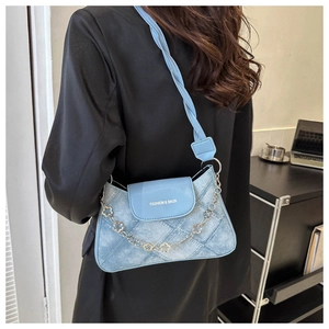 Détail du sac à bandoulière en denim bleu avec chaîne trèfle dorée et lettrage fashion
