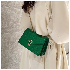 Detail of green crocodile-pattern crossbody bag with gold U-shaped metal lock and chain