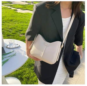 Borsa a secchiello a tracolla in pelle bianco crema mostrata su modella in ambiente esterno