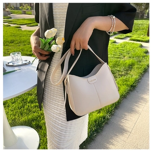 Dettaglio della borsa a tracolla in pelle beige con etichetta FASHION indossata da modella