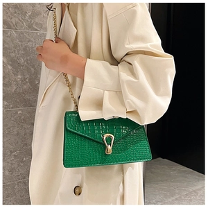 Detail of green crocodile embossed shoulder bag with gold metal lock and chain strap