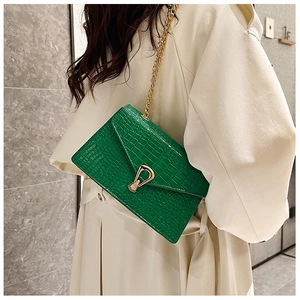 Close-up of green crocodile texture shoulder bag with gold horseshoe buckle on beige coat
