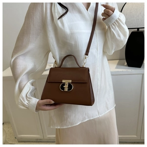 Close-up of brown leather crossbody bag featuring gold metal swivel lock and top handle