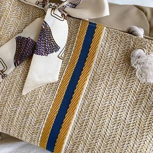 Detail of woven straw tote bag featuring contrast stripes and elegant printed silk scarf