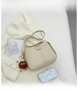 Dettaglio borsa a tracolla crema minimalista con placca fashion e ciondolo in peluche marrone