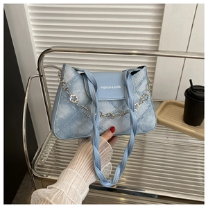 Détail du sac à bandoulière en denim bleu avec chaîne florale et poignée tressée
