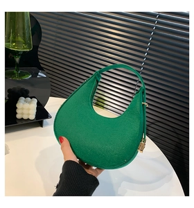 Dettaglio borsa a mezzaluna verde con texture a grana fine e cerniera dorata lucida