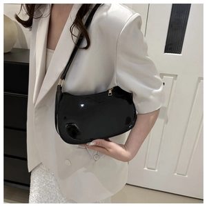 Close-up of black patent leather underarm bag with glossy finish and gold metal zipper