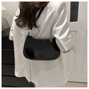 Sac porté épaule en similicuir brillant noir sur le fond d'un blazer blanc chic