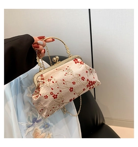 Detailed close-up of champagne silk handbag with red plum blossom embroidery and gold handle
