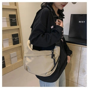 Close-up of beige nylon half-moon crossbody bag with woven knot detail and wide strap